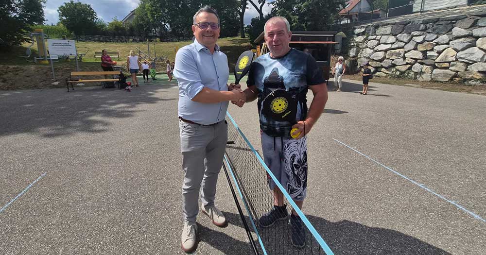Bürgermeister und Pickleball-Spieler schütteln sich auf einem Sportplatz in Österreich die Hände.